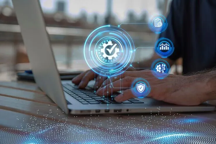 Hands on laptop typing with holographic cybersecurity check, analytics, and shield icons.